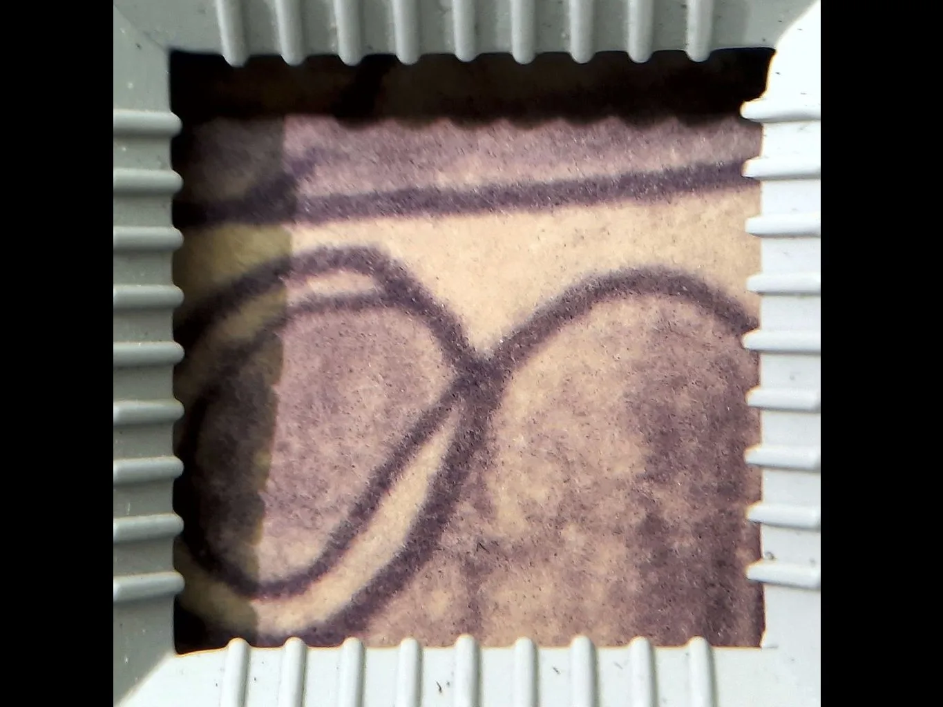 Detalhe de um papel creme com traços pretos e preenchimento arroxeado, dentro de esquadro branco quadrado