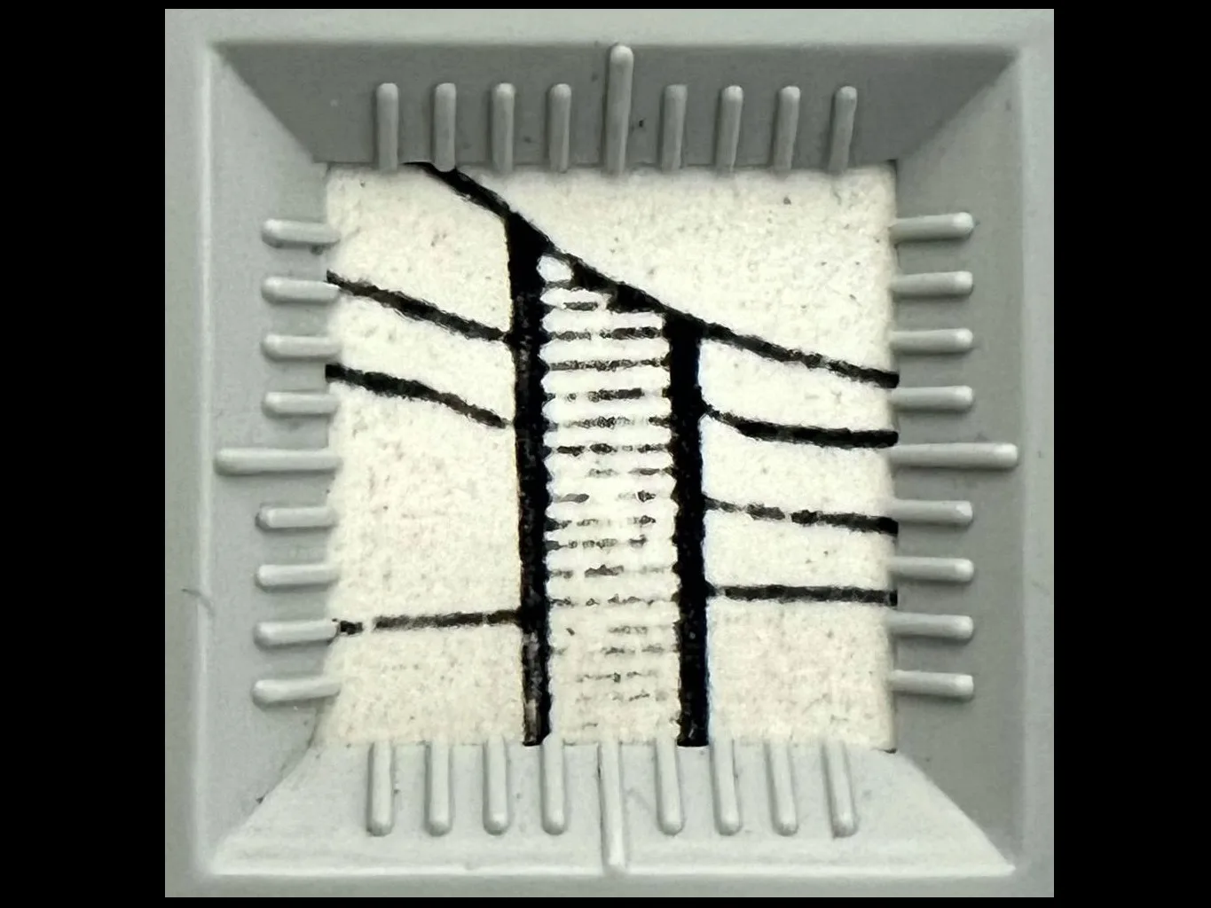 Detalhe de um papel branco com traços pretos perpassando uma coluna tracejada, dentro de um esquadro branco quadrado