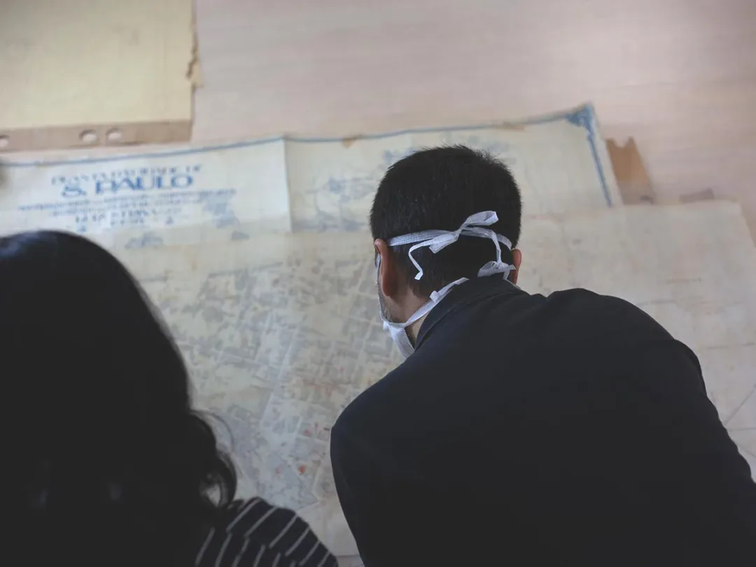 Foto de um mapa da cidade de São Paulo sendo observado por um homem de máscara e por uma mulher de cabelo escuro