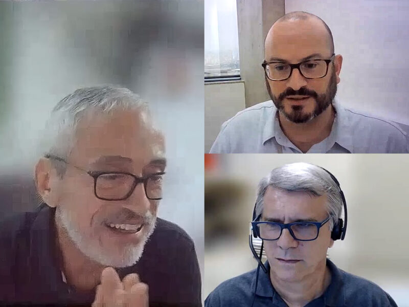 3 homens brancos de meia idade, de óculos, em videoconferência: à esquerda um grisalho de barba, à direita: acima um careca de barba escura e abaixo um grisalho usando fone de ouvido.